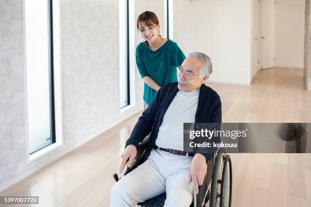 父親が車椅子で部屋を動き回るのを手伝っている若いアジア人女性。 - 介護施設 ストックフォトと画像
