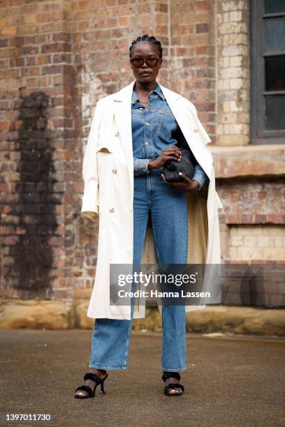 Malaan Ajang wearing Zara white trench, denim Jumpsuit, black heels and black clutch at Afterpay Australian Fashion Week 2022 on May 13, 2022 in...