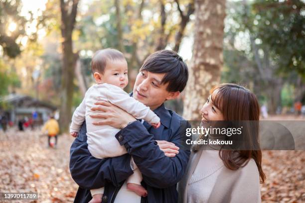 portrait of a young couple and their baby smiling in a park. - young couple with baby stock pictures, royalty-free photos & images