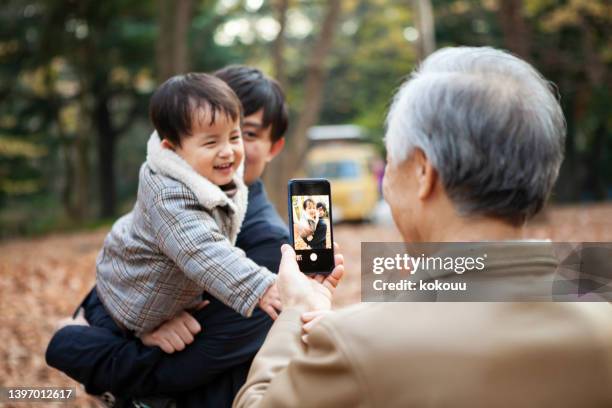 息子を抱っこする父親と祖父がスマホで撮影している。 - 父の日　日本 ストックフォトと画像