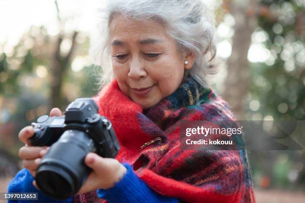 senior woman enjoying digital camera photography in nature. - woman in a shawl stockfoto's en -beelden