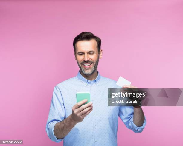 man holding credit card using smart phone - happy man pink background stock pictures, royalty-free photos & images