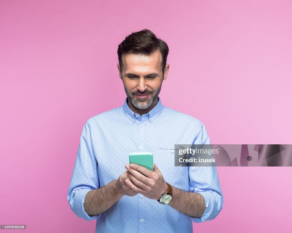 Man using mobile phone against pink background