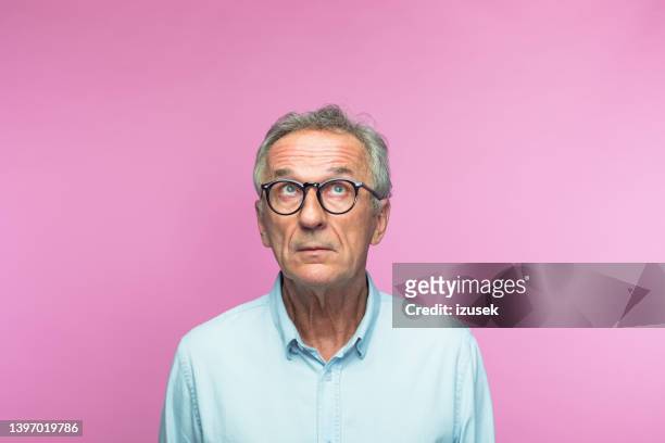 nachdenklicher älterer mann im ruhestand, der nach oben schaut - portrait colour background stock-fotos und bilder