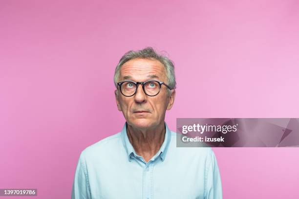 nachdenklicher älterer mann im ruhestand, der nach oben schaut - senior studio portrait stock-fotos und bilder