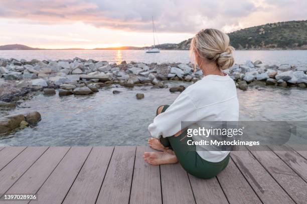 jeune femme sur une jetée au-dessus de la mer regardant le coucher du soleil - ponton mer photos et images de collection