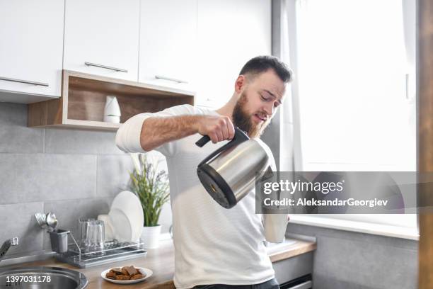 handsome male pouring himself coffee in kitchen - kettle stockfoto's en -beelden