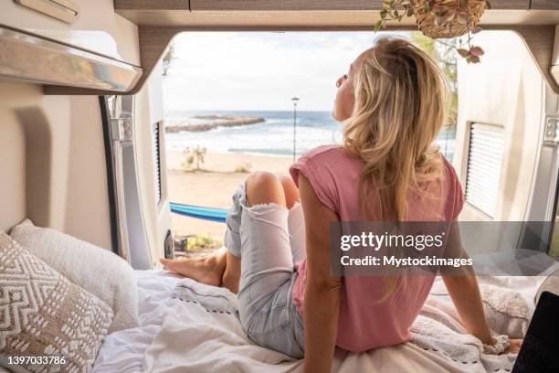 woman lying at the back of a van looking at ocean, solo traveler in camper van - woman back pillow blonde stock pictures, royalty-free photos & images