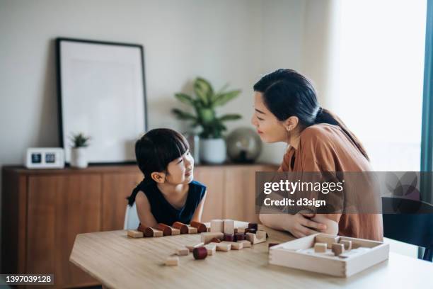 young asian mother and little daughter having fun playing wooden building blocks together, chatting and smiles at each other. enjoying mother and daughter bonding time at home - hong kong girl stock-fotos und bilder