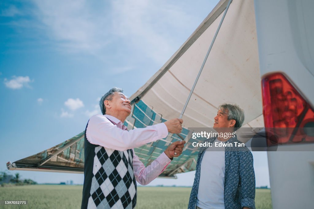 2 asiatischer chinesischer älterer Mann, der tagsüber neben dem Reisfeldfeld ein Markisendach des Wohnmobils aufstellt
