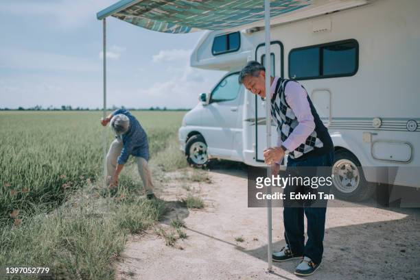 2 ancianos chinos asiáticos instalando toldo de autocaravana durante el día junto al arrozal