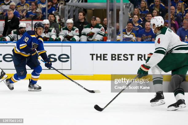 Brayden Schenn of the St. Louis Blues skates with the puck while under pressure from Jon Merrill of the Minnesota Wild during the first period in...