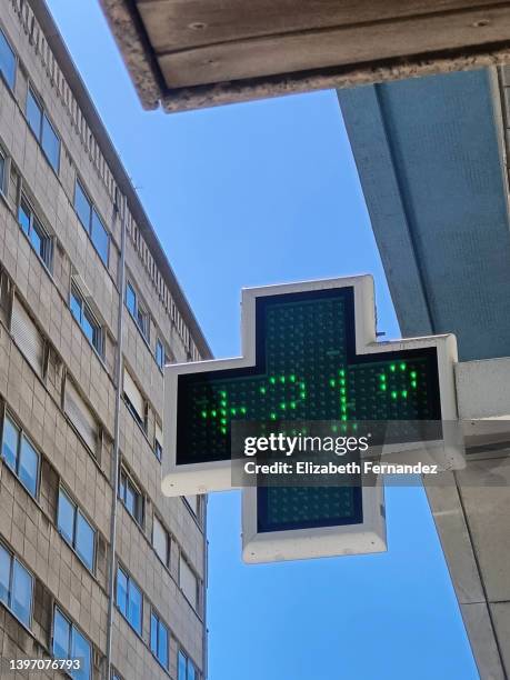 a streetside digital thermometer indicating 21 degrees at pharmacy sign - cross symbol stock-fotos und bilder