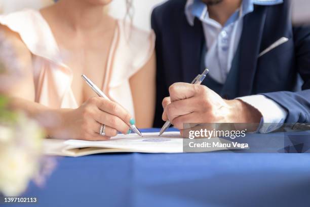 close-up view of man and woman signing marriage certificate, she wears a vintage wedding dress and he wears a formal suit. - casados fotografías e imágenes de stock