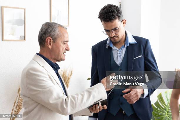 a man giving a watch to his newly married son as a gift at the registry office - build presents suits photos et images de collection