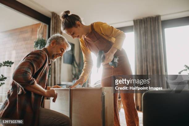 father and teen daughter assembling new furniture in the renovated apartment - diy stock-fotos und bilder