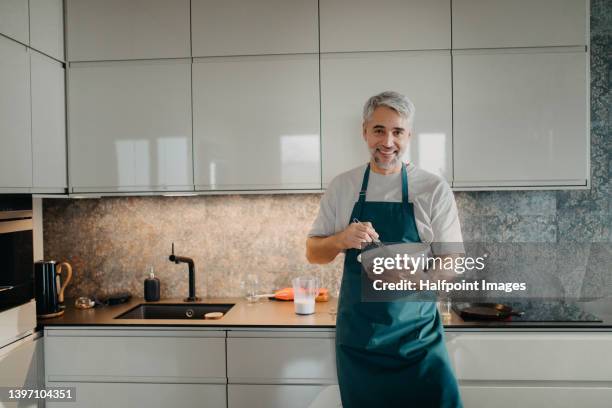 cheerful mature man cooking in kitchen at home. - mixing bowl stock pictures, royalty-free photos & images