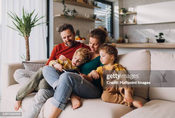 little children bonding with parents on sofa at home and using tablet. - happy children foto e immagini stock