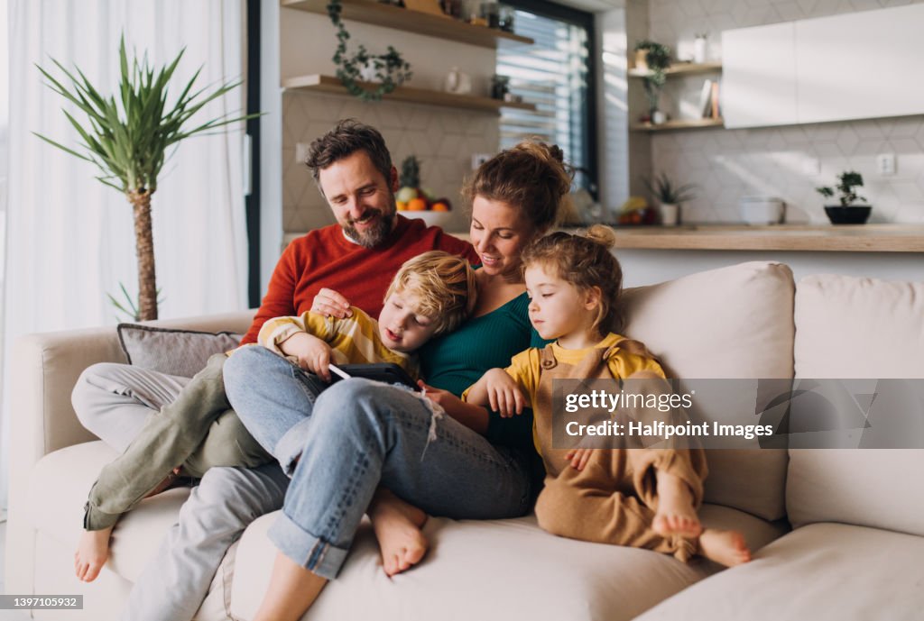 Little children bonding with parents on sofa at home and using tablet.
