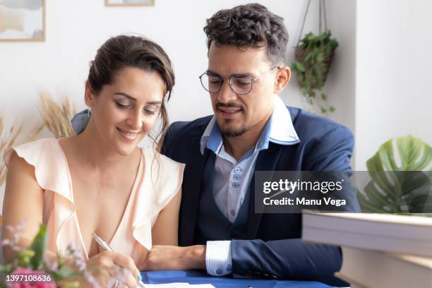 beautiful bride looking radiant as she signs the marriage license with her husband. - marriage certificate stock pictures, royalty-free photos & images