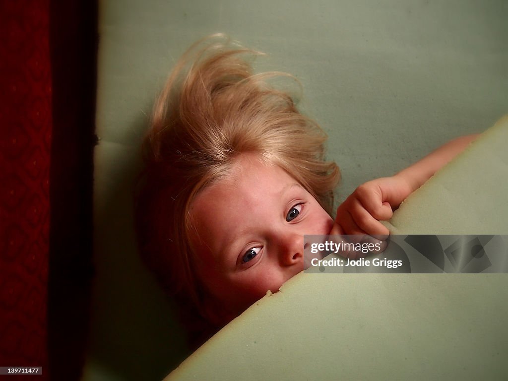 Young child hiding under piece of foam