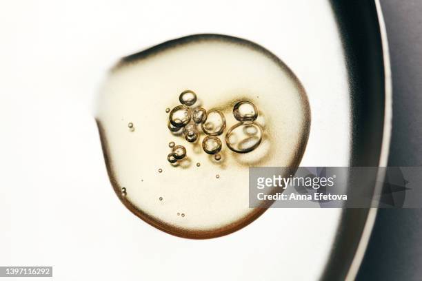 drop of essential oil with bubbles on a metal plate on gray background. concept of dermatological treatment of different skin conditions. macro photography from above - ホホバ ストックフォトと画像