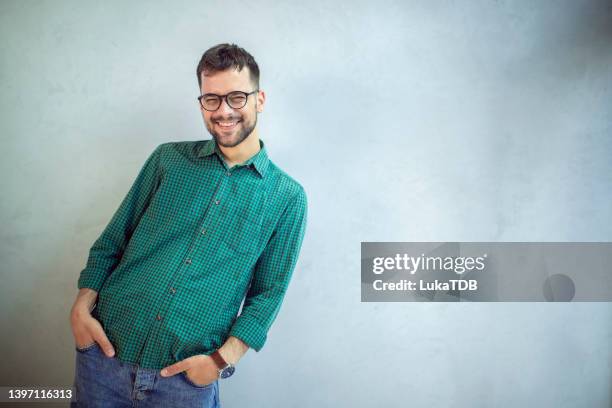 ein lächelnder mann mit den händen in den taschen, der vor weißem hintergrund steht. - grünes hemd stock-fotos und bilder