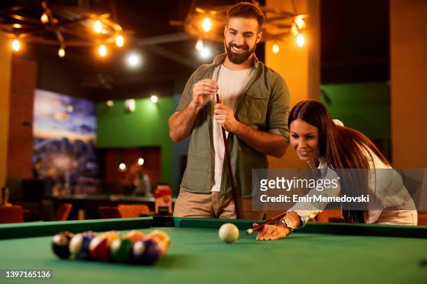 jovem casal desfrutando de jogar um jogo de sinuca em um salão de sinuca local - snooker - fotografias e filmes do acervo