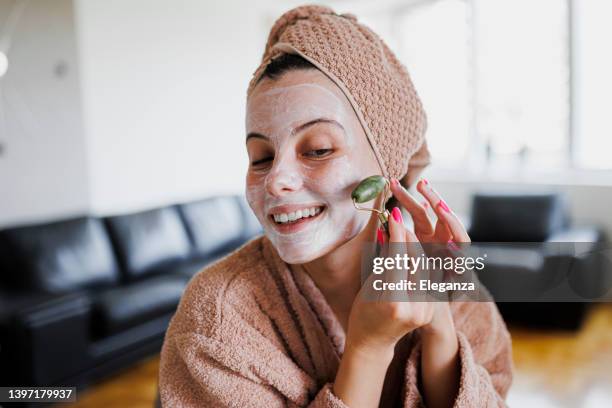 woman using jade roller on her face at home. young girl massaging face by jade roller. self-care facial massage, anti-aging lifting skincare procedure - jade gema imagens e fotografias de stock