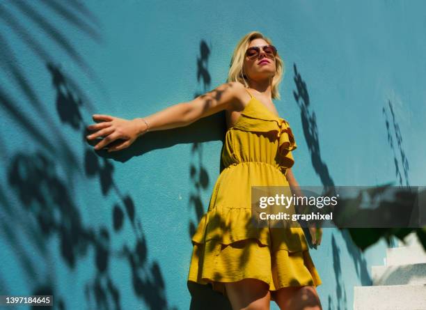 portrait de femme souriant contre le mur à l’ombre d’un palmier - robe jaune photos et images de collection