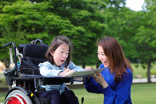 Asian girl in wheelchair and her mother drawing in sketchbook