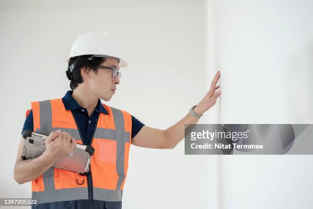 monitoring interior wall inspections within a virtual environment. male japanese construction engineer is final inspection of the surface a interior wall during the house building delivery. - flat inspection fotografías e imágenes de stock
