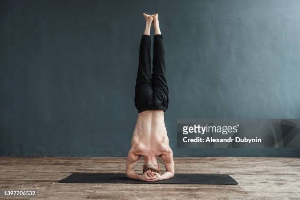 experienced yogi doing yoga with headstand support in the gym. caucasian man practices advanced yoga. yoga concept. - yogi stock-fotos und bilder
