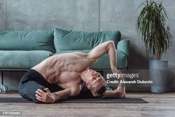 yogi man doing yoga exercise at home near the sofa practicing body stretching on the floor - yogi stock-fotos und bilder