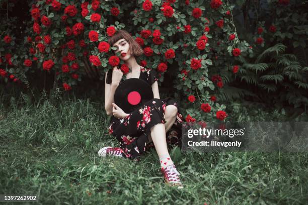 hintergrund der sommernatur. mode brünettes modell. frühlingsrosenblumengarten. fabelhafte frau mit roten lippen im kleid. tolle blumenwand. retro-dame. frauenporträt. trendiger look. moderne kunst - summer sounds stock-fotos und bilder