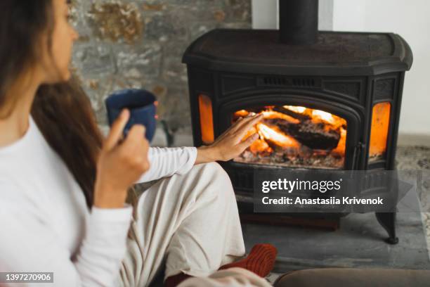 woman's hand holding cup of hot drink in front of fireplace in cozy home. - fireplace stock pictures, royalty-free photos & images