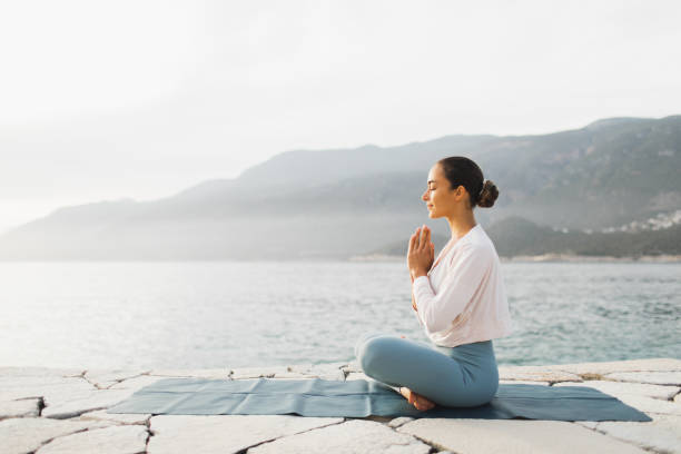 young woman praying and meditating outdoors by seaside. self care and mindfulness, menthal health. awakening in morning - morning prayer stock pictures, royalty-free photos & images