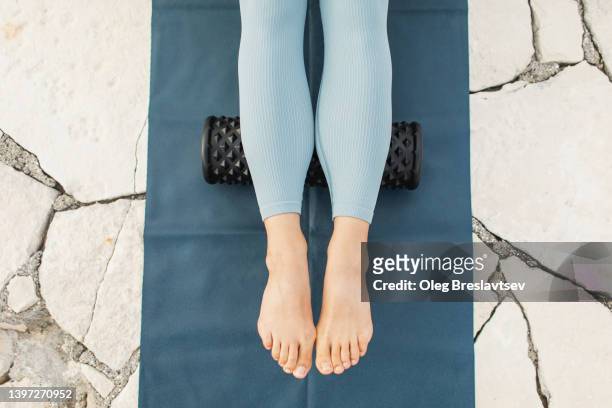woman massaging legs and calf muscles with black massage roll. roller massager, self massage and healthy lifestyle - kuit menselijk been stockfoto's en -beelden
