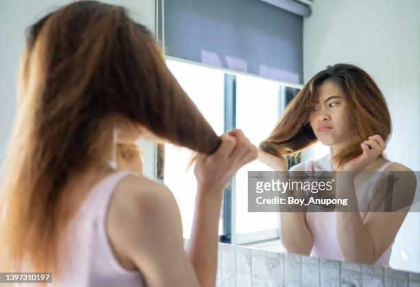 unhappiness asian woman while she saw her messy hair in the mirror after waking up in the morning. - cheveux secs photos et images de collection