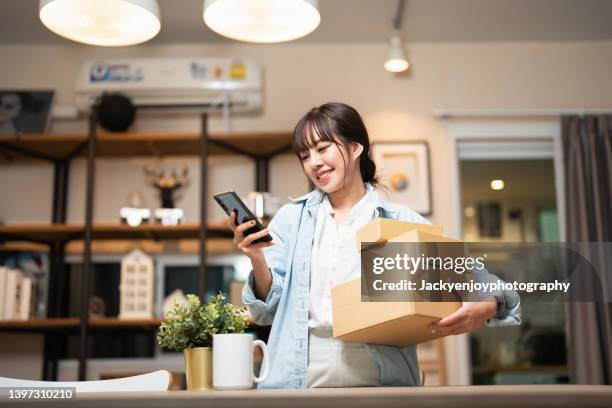 beautiful young woman with smartphone receiving parcel purchased online - compras em casa imagens e fotografias de stock