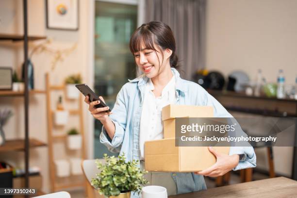 a young asian woman is sitting at home, using her credit card and phone/laptop to make an online shopping transaction. - webshopper stock-fotos und bilder