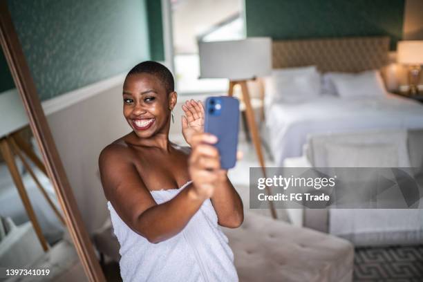 woman using mobile phone doing a video call (or taking a selfie) wearing a towel at home - bedroom vanity stock pictures, royalty-free photos & images