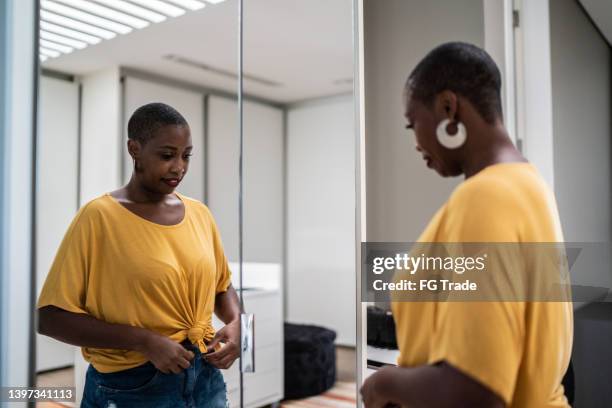 mid adult woman arranging clothes looking in the mirror at home - black trousers stockfoto's en -beelden