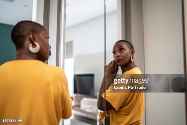 mujer mediana adulta poniéndose pendientes mirándose en el espejo de casa - earring fotografías e imágenes de stock