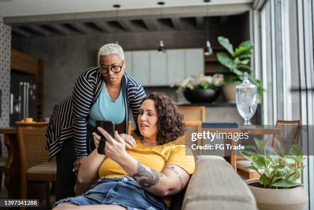 female friends talking and using the mobile phone at home - sending stock pictures, royalty-free photos & images