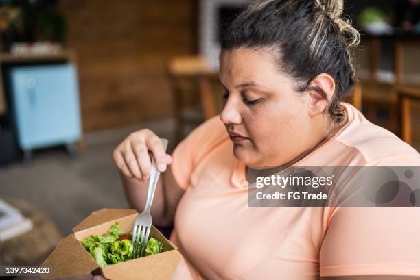 mid adult woman eating salad at home - obesitas stockfoto's en -beelden