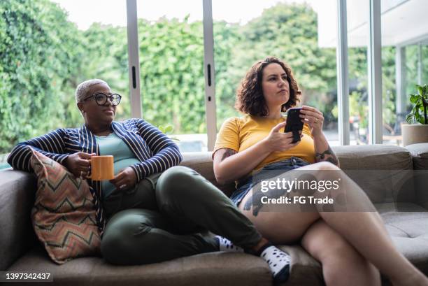 female friends watching tv and using mobile phone at home - fat lesbian stock pictures, royalty-free photos & images