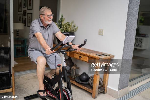 hombre mayor usando bicicleta de ejercicios en casa - exercise bike fotografías e imágenes de stock