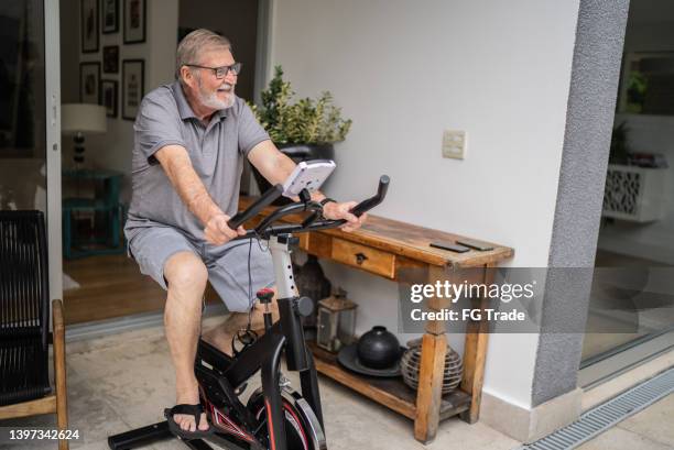 senior man using exercise bike at home - exercise bike stock pictures, royalty-free photos & images