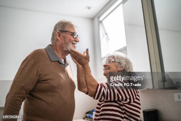 senior woman taking care of her husband in the bathroom at home - bathroom senior stock pictures, royalty-free photos & images